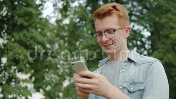 帅哥学生在公园户外使用智能手机微笑享受设备视频的预览图