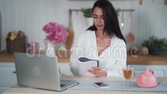 穿着浴袍的年轻女子坐在厨房里写日记侧视视频的预览图
