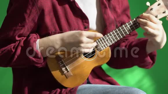 在一个绿色的背景下年轻的希普斯特女人演奏尤库莱吉他视频的预览图