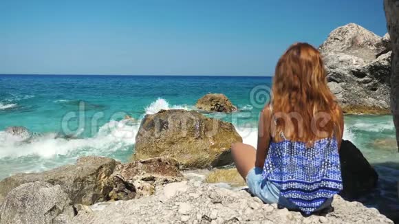 旅游女孩看着海浪缓慢地拍打着岩石视频的预览图
