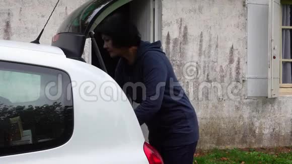 成熟的黑发女人从汽车后备箱里卸下购买物品视频的预览图