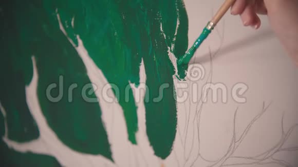 一个年轻的女人她的手在画布上画一棵绿树视频的预览图