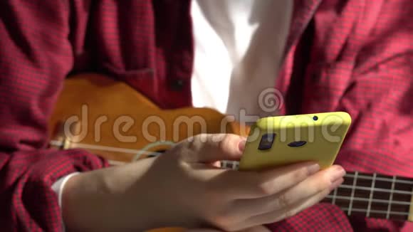 年轻的时髦女人弹着四弦琴吉他一个女人在智能手机上读一首歌4K视频的预览图