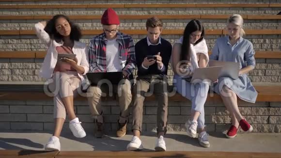 多民族学生坐在一起被电话电脑标签吸引设备成瘾视频的预览图