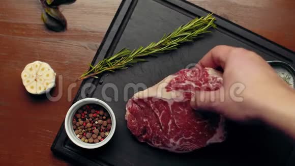 一个男人手把一块大理石切割的牛排放在切割板上旁边是大蒜迷迭香迷迭香一杯香料视频的预览图