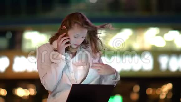 在一个刮风的夜晚一个手提电脑的女商人坐在外面打着一个富有表现力的电话视频的预览图