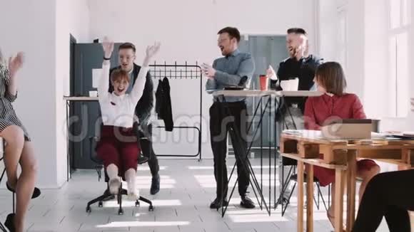 红色EPICW笑的年轻商务女性庆祝成功与快乐的办公室同事骑椅子慢动作视频的预览图