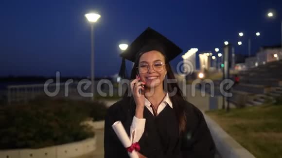 穿着黑色毕业礼服的年轻学生在电话里走来走去视频的预览图