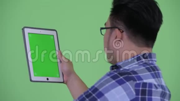 使用数码平板电脑的快乐年轻超重亚洲时髦男人的后视图视频的预览图