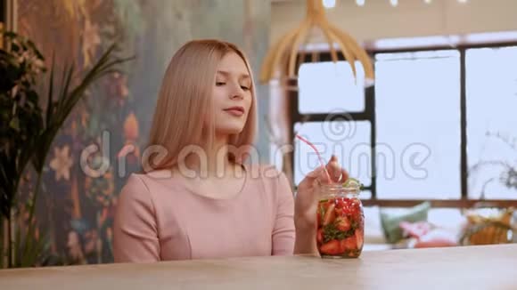 年轻漂亮的女孩从一个玻璃罐子里喝草莓柠檬水在酒吧柜台后面有一根稻草视频的预览图