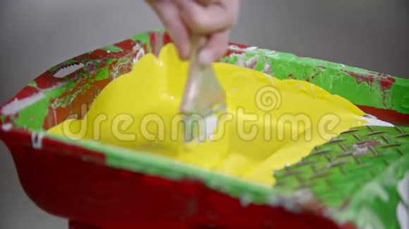 一个人把刷子淹死在油漆盘里的黄色油漆里视频的预览图
