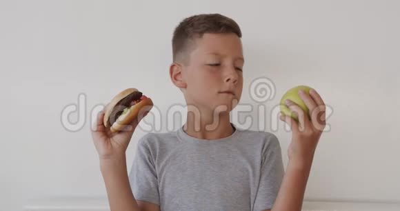 男孩选择健康或不健康的食物男孩在苹果和汉堡之间做出选择健康还是快速垃圾食品选择了视频的预览图