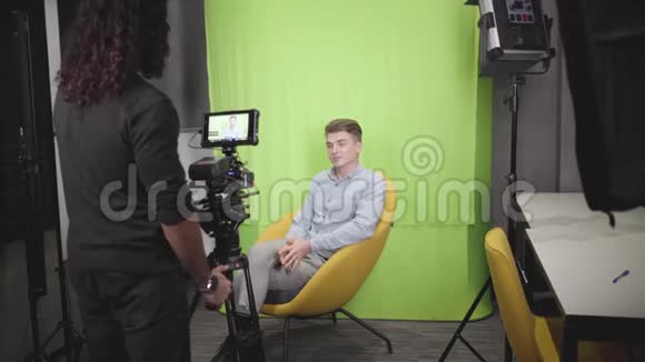 年轻的积极的白人男子坐在黄色的扶手椅上在镜头前交谈摄像师录制视频成功视频的预览图