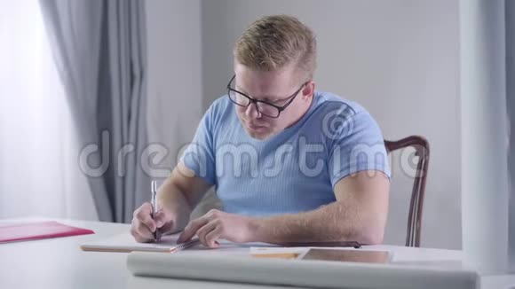 一幅自信的白种人商人戴眼镜坐在桌子旁做笔记的肖像红头发的人在思考视频的预览图