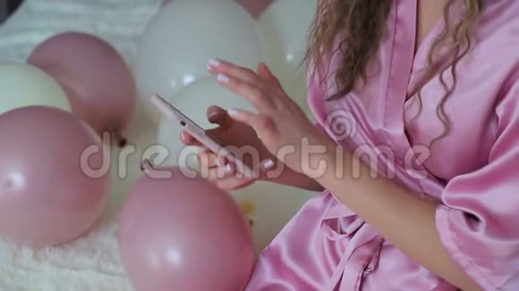 女孩的手把电话握在手里一个穿着粉红色长袍的女孩在节日的房间里拿着气球视频的预览图