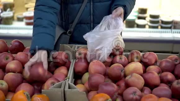 一个女人在商店里选择红苹果把它们放进玻璃纸包里超市里的顾客概念特写视频的预览图