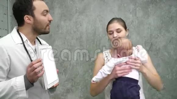 医生在药片上向母亲和婴儿展示医疗结果白色显示器视频的预览图