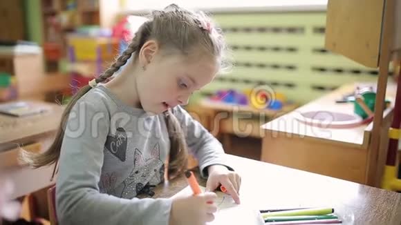 一个女孩在幼儿园里坐在一张桌子上画一幅画视频的预览图