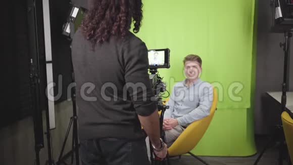 白种人年轻人坐在黄色扶手椅上对着镜头说话的肖像摄像师录制视频博客视频的预览图
