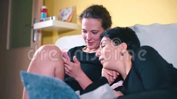 两个姐妹在家里躺在沙发上看着智能手机的屏幕视频的预览图