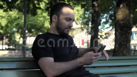 年轻的帅哥坐在长凳上通过电话浏览互联网视频的预览图