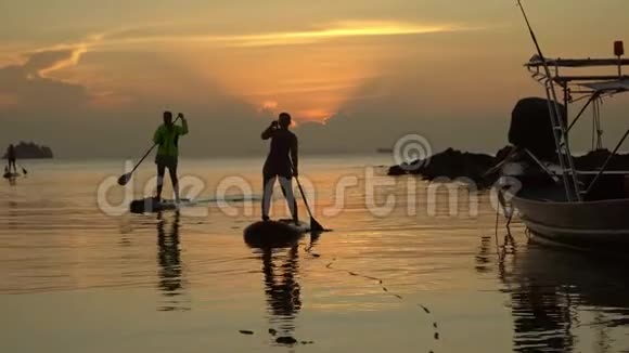 傍晚夕阳西下的海洋热带景观两个人在冲浪板上游到岸边视频的预览图