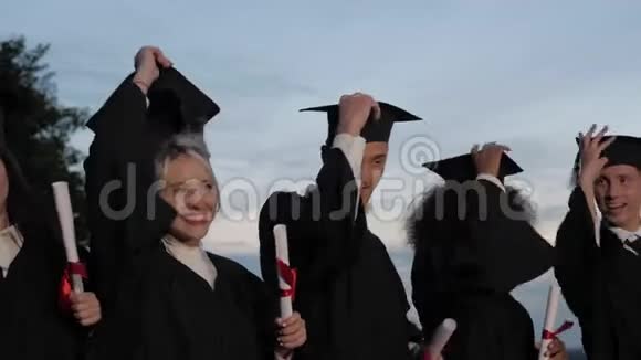 快乐而兴奋的混合种族的学生朋友在毕业典礼上边走边扔帽子视频的预览图