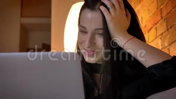 在家里的气氛中年轻的黑发白种人女孩在沙发上观看笔记本电脑的特写镜头视频的预览图
