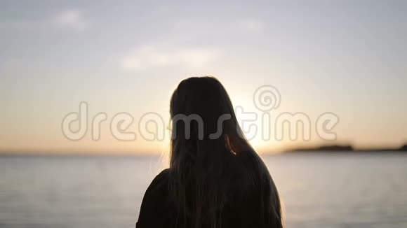 一个留着长发的女孩在夕阳的背景下走到湖岸视频的预览图