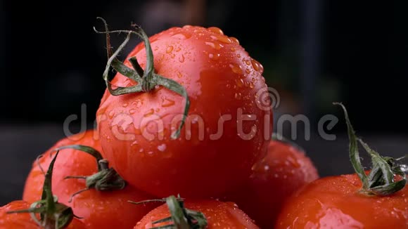 男人在黑暗的背景上带着水滴的红番茄在近景中耕作和烹饪视频的预览图