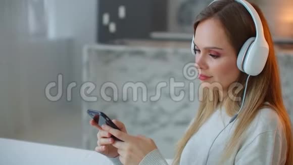 快乐的美国青少年在家里的沙发上用智能手机放松年轻女子晚上在手机上撒乐视频的预览图