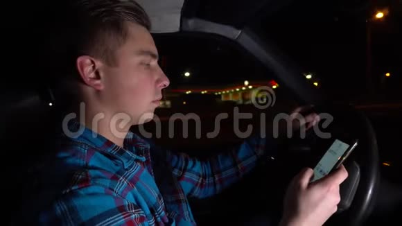 一个年轻人开着车在电话上写了一条信息一天中的夜晚司机侧视视频的预览图