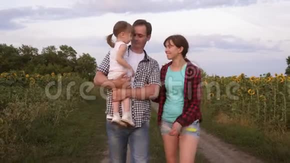 一家人带着一个小宝宝带着向日葵在田野里走来走去笑着农业女孩母亲和父亲视频的预览图