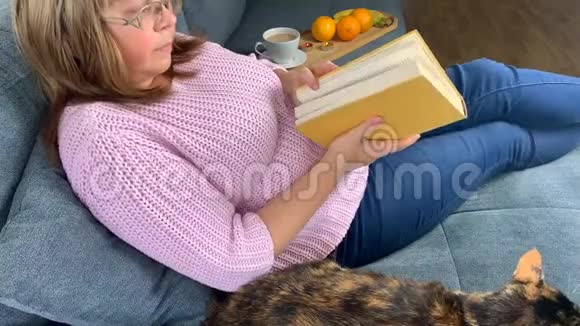 房间里的沙发上一个穿着粉红色套头衫的女人坐着看书喝咖啡旁边躺着一个美丽的黑暗视频的预览图