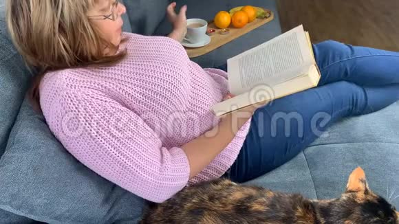 房间里的沙发上一个穿着粉红色套头衫的女人坐着看书喝咖啡旁边躺着一个美丽的黑暗视频的预览图