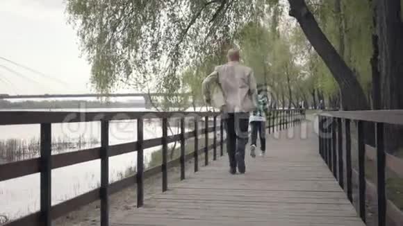 小男孩在河边的木桥上从爷爷身边跑开老人累了停下来视频的预览图