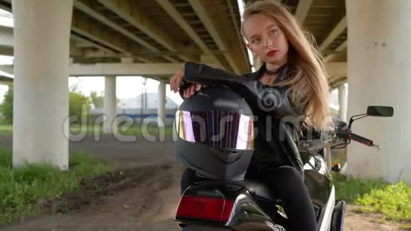 骑摩托车坐在城市桥下戴着摩托头盔的比基尼女孩穿黑色皮夹克的摩托女孩视频的预览图