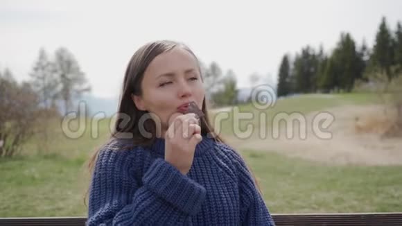 穿着蓝色毛衣的漂亮女孩在阿尔卑斯山吃一块美味的瑞士巧克力视频的预览图