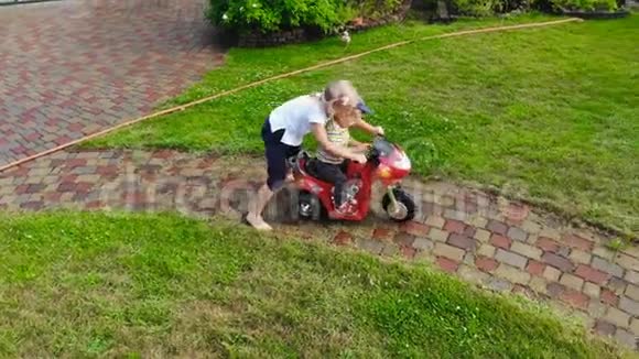 两个可爱的金发碧眼的孩子在花园小径上玩电动玩具自行车兄弟姐妹享受视频的预览图