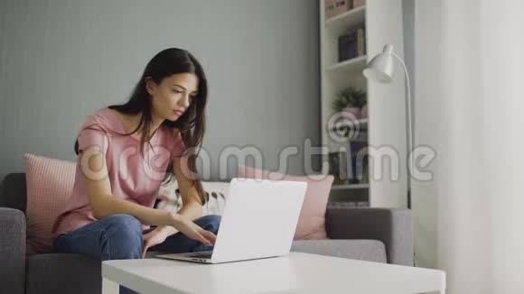 女人看新闻用看家里的笔记本电脑坐在沙发上年轻的家庭主妇视频的预览图