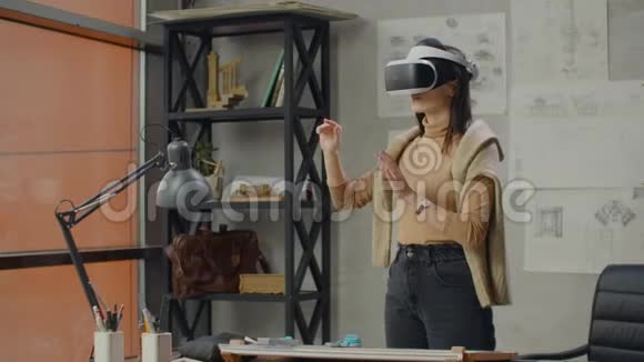 办公室里戴着虚拟现实头盔的女工程师用手势来管理项目而不离开办公室视频的预览图