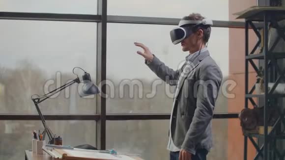男工程师在一个虚拟现实头盔附近的大窗口用手模仿的工作界面视频的预览图