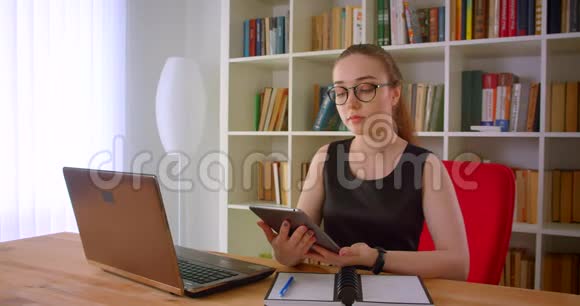 年轻漂亮的红发女商人戴眼镜的特写照片用平板电脑向坐在里面的照相机显示绿色屏幕视频的预览图