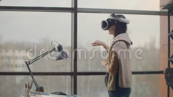 一名戴着虚拟现实头盔的女工程师在大窗户附近用手模拟界面的工作视频的预览图