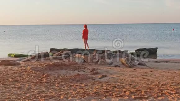 孤独的女人穿着红色的t恤站在岸边的石头上等待日出视频的预览图
