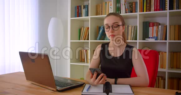 年轻漂亮的红发女商人戴着眼镜用手机显示绿色屏幕拍摄坐在里面的照片视频的预览图