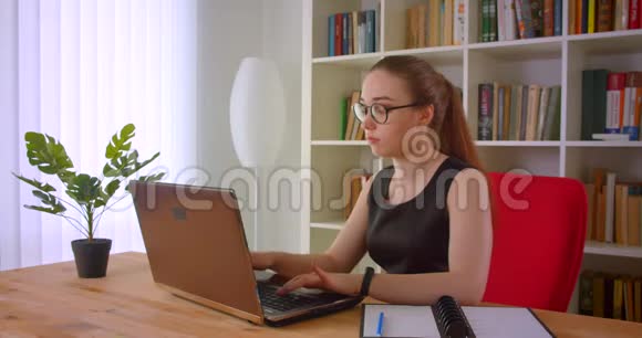 在办公室里戴着笔记本电脑的戴着眼镜的年轻无聊漂亮红发女商人的特写照片视频的预览图