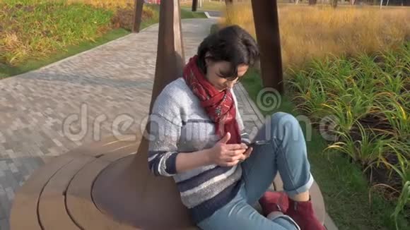 白种人女人坐在公园的圆凳上手里拿着电话视频的预览图