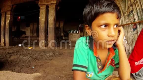 在瓦拉纳西的背景贫民窟里一个小印度男孩用火柴清理耳朵黑黑的牛棚视频的预览图