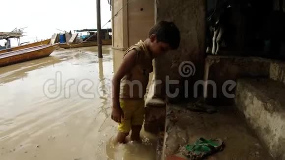 小印度男孩在洪水泛滥的恒河贝顿楼梯上的脏水里洗脚牛船的蹄子在码头上的拖鞋上牛屎视频的预览图